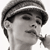Black-and-white pixelated close-up of a person's face with short dark hair, wearing a cap or headband, and holding an object near the mouth.
