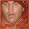 A static image of a person with light skin and blue eyes wearing a red hooded garment with white patterns, with red text reading RANDY ORTON at the bottom.