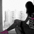 Pixelated figure in black outfit with purple accents seated against light background, legs crossed and arms resting on knees.