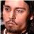Pixelated close-up of a person's face with light skin tone, dark eyebrows, and visible stubble, set against a dark background with subtle light reflections.