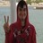 A person in a red hooded garment making a peace sign with their right hand against a blurred background.