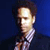 Pixelated image of a person with light skin tone, dark hair, and a checkered shirt against a dark blue background.