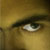 A close-up of a human eye with a light brown iris, dark eyelashes, and a visible eyebrow, set against a blurred golden-brown background.