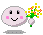Pixelated pink circular character with black eyes, pink cheeks, and a smiling mouth holding a bouquet of yellow, white, orange, and green flowers against gray background.