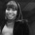 Black-and-white image of a person wearing a cap and dark jacket over a light shirt, with a blurred background.