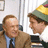 Pixelated image split into two sections: left shows two men in indoor setting, right displays green background with yellow text.