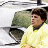 Pixelated static image of a person in yellow clothing holding a green object against a white background with gray border elements.