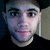A pixelated image of a person with dark hair and light skin, wearing a black shirt against a neutral background.