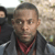 A pixelated static image shows a person with short dark hair wearing a dark jacket and red bandana, standing outdoors with another figure partially visible to the left.