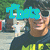 A person wearing dark sunglasses and a black shirt with yellow text stands outdoors, with pixelated blue text overlays changing across frames.