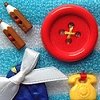 Static image of five distinct objects on a blue textured background: two brown cylindrical items, a large red button, a white bow, a blue fabric piece, and a yellow telephone-shaped item.