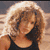 Pixelated image of a person with light brown hair wearing a dark sleeveless top against a blurred background.