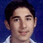 Pixelated portrait of a person with dark hair and light skin wearing a white collared shirt against a blue background, with pixelated text reading 'brandon is so awsone' on a black background.