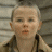 Pixelated close-up of a child with light skin and short light hair wearing a dark jacket over a light shirt against a blurred background.