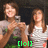 Two people in a pixelated image with green text [lol] at the bottom, one holding a camera, both wearing light-colored tops against a dark background.