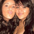 Two identical figures with light skin and dark hair pose closely together against a dark background, one figure's hand near the other's face.