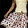 A person wearing a light-colored sleeveless top and a patterned skirt with brown, black, and white shapes on a light background.