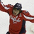 A person in a red sports jersey with white and dark blue accents raises both arms, head tilted down.