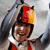 Static 50x50 pixel icon showing a stylized figure in red and white attire with dark hair, holding a tennis racket against a gray background.