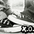 Black-and-white pixelated image of a figure in mid-kick pose with blurred motion lines, set against abstract background shapes and featuring 'X.0' text at bottom right.