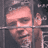 Pixelated static image of a person behind metal bars with one hand raised, rendered in pinkish-brown tones against dark background.