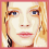 Pixelated of four showing a blonde woman's face with blue eyes, red lips, and dark earrings against pink borders