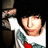 Pixelated image of a person with dark hair wearing a white shirt with green and red patterns, holding a white object against a dark background.