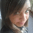 A pixelated image of a person with brown hair and light skin, wearing a dark top with white accents, against a blurred background.