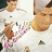 A person in a white shirt with a pink and white patterned design holds a brown object near their face, with a blurred background.