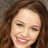 Pixelated close-up of a person with brown hair and light skin, smiling slightly against a dark background.