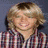 Pixelated static image of a person with light brown hair wearing a checkered shirt against a dark blue background.