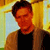 Pixelated image of a person with short dark hair wearing a black shirt and brown jacket against a yellow and light blue background.