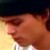 Pixelated close-up of a person's face with warm skin tones, dark hair, and a light-colored checkered shirt against a gradient background.