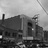 Black-and-white pixelated image of a building with multiple windows and a chimney under a cloudy sky.