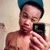 A pixelated image of a shirtless person wearing a blue cap, holding a black rectangular object near their face against a light background.