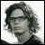 Pixelated grayscale portrait of a person with dark curly hair, neutral expression, and light background.