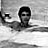 Black-and-white pixelated image of a person with short hair and dark sunglasses in water, viewed from the shoulders up against a blurred background.