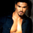Pixelated static image of a shirtless man with short hair and facial stubble wearing a dark blue jacket, set against a black background.