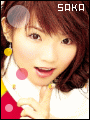 A person with brown hair and yellow earrings wears a white and red outfit with pink circular accents, making a finger gesture under the text 'SOKO' in the top-right corner.