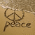 Sand drawing of peace symbol with 'peace' text, blue flip-flops on light background, dolphin jumping over water at sunset.