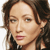 Pixelated close-up of a person with brown hair, light skin, and pink lips, wearing a dark top with a white collar.
