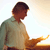 Pixelated image of a person in profile wearing a light green shirt, dark pants, and a dark cap, standing against a bright sky with a golden horizon line.