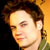 Pixelated close-up of a person's face with brown hair and light skin, set against a gradient background transitioning from dark on the left to yellow-orange on the right.