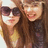 Two women with long brown hair pose together; one wears dark sunglasses, the other has a smiling expression.