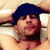 Static pixelated image of a person wearing a dark blue cap and red shirt, lying down with arms behind head against light-colored background.
