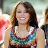 A woman with shoulder-length brown hair smiles, wearing a sleeveless top with multicolored sequined stripes over a white undershirt.