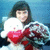 A person holds a white teddy bear with red accents against a blue background, wearing a patterned garment.