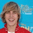 Pixelated image of a person with brown hair wearing a red jacket over a white shirt against a blue background with light blue and white shapes.