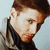 Pixelated close-up of a person with brown hair and light skin wearing dark clothing against a pale blue background.
