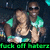 Two people in green shirts pose together with one person giving a thumbs-up gesture, set against a dark background with pixelated text at the bottom.
